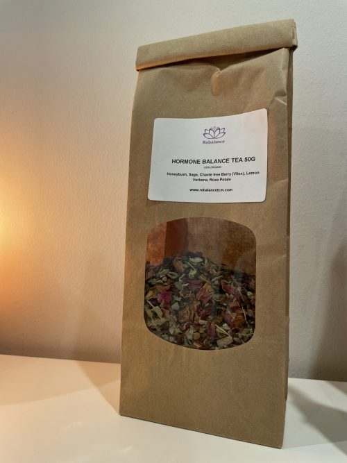 A bag of Hormone Balancing Tea sitting next to a candle on a table.