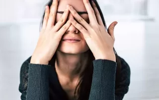 A woman practicing self-care by covering her eyes with her hands.